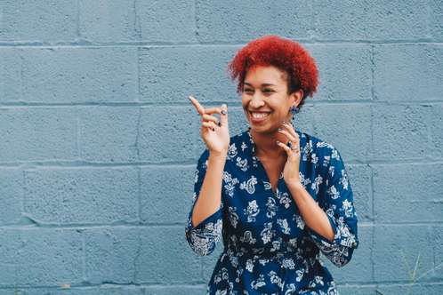 Smiling woman with red hair pointing to the side against a blue wall
